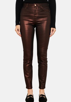 Slim-fit metallinväriset ruskeat housut, joita yhdistetään mustaan pitkähihainen toppiin ja mustiin loafers-kenkiin, joissa on kultaiset solkisomisteet, kuvattuna vyötäröstä jalkoihin.