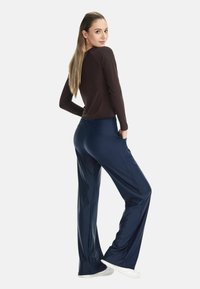 Braunes Langarmshirt kombiniert mit navyblauen, weit geschnittenen Hosen und weißen Turnschuhen. Das Oberteil ist figurbetont, die Hose hat seitliche Taschen.