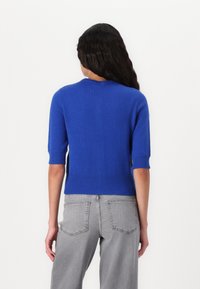 Suéter azul de manga corta con cuello y dobladillo acanalados. Textura suave, diseño ajustado, combinado con jeans de tiro alto en gris claro.