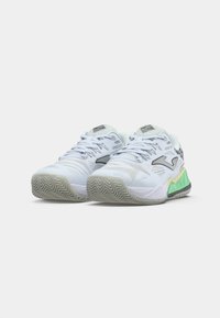 Baskets de sport blanches avec un dessus en mesh texturé, accents noirs et verts, et une semelle extérieure à motif en zigzag. Comprend un col et une languette rembourrés.