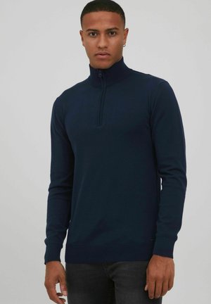 Marineblauer Pullover mit hohem Kragen, halbem Reißverschluss, langen Ärmeln und gerippten Bündchen. Hergestellt aus einem weichen, strukturierten Stoff.