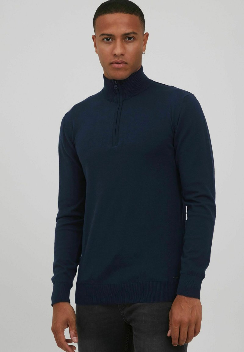 Suéter de punto azul marino con alto cuello, cierre de media cremallera, mangas largas y puños acanalados. Fabricado en un tejido suave y texturizado.