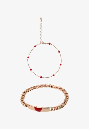 Hieno kultainen ketjurannekoru, jossa on pieniä punaisia helmiä, ja paksumpi kultainen ketjurannekoru, jossa on punaisen huulimuotoisen riipuksen.