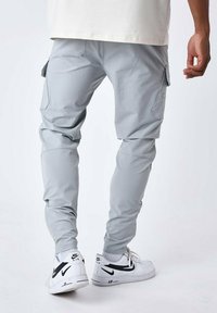 Pantalones cargo grises con piernas ajustadas, bolsillos laterales y puños elásticos, combinados con zapatillas Nike blancas con detalles en negro.