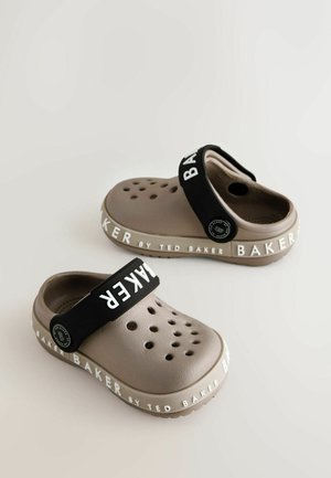 Kaks pruuni kummist sabat, ventilatsiooniaukudega, must reguleeritav rihm, millel on pressitud "BAKER" ning valge logo tekst tallal.