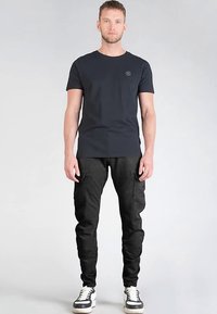 Zwart t-shirt met korte mouwen en ronde hals met een klein logo, gecombineerd met zwarte cargobroek en sneakers met een witte zool.