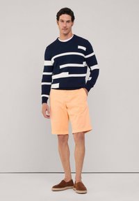 Jersey de color navy con rayas horizontales blancas, combinado con pantalones cortos melocotón. El modelo lleva zapatos tipo slip-on marrones. Fondo neutro.