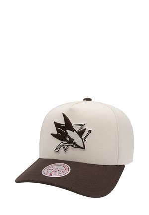 Casquette de couleur crème avec une visière marron. Présente un logo de requin en noir et gris sur le devant. Conçue en tissu avec un design structuré.