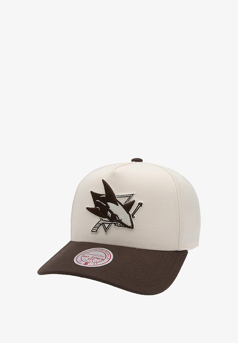 Cream-colored cap with a brown brim. Features a shark logo in black and gray on the front. Crafted from fabric with a structured design.
