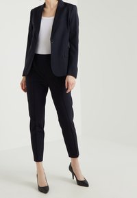 Marinblå blazer med en knapp, parat med figursydd marinblå byxor och svarta spetsiga klackar, vilket skapar en skräddarsydd och polerad look.