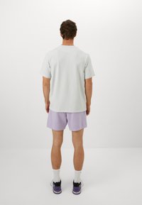 Lichtgrijze textuur t-shirt en lichtpaarse shorts, met een ontspannen pasvorm, gedragen met witte sokken en zwart-paarse sneakers.