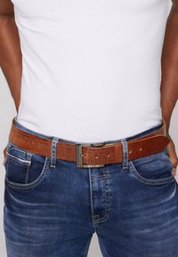Brown leather belt with a textured finish, featuring a metallic silver buckle, worn with a white t-shirt and blue jeans.