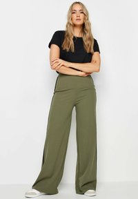 Pantaloni a gamba larga in tessuto verde oliva con dettagli laterali. In abbinamento a una maglietta nera aderente e sneakers bianche. Design semplice e informale.