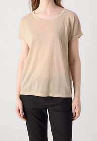 Top semitranslúcido en color beige, de manga corta y con un amplio cuello redondo. Textura suave y ajuste holgado. Combinado con pantalones negros.