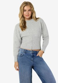 Suéter cropped en gris claro con textura acanalada y cremallera en el frente, combinado con jeans azules holgados. Las mangas son largas y ligeramente abullonadas.
