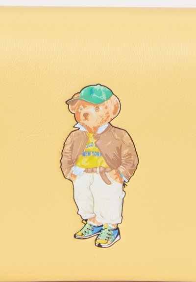 Yellow leather background with an illustrated bear wearing a green cap, brown jacket, yellow t-shirt, white pants, and multicolored sneakers.
