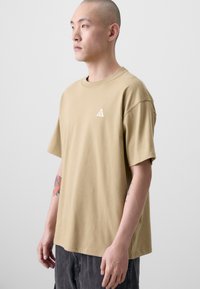 Khaki kortærmet T-shirt lavet af blød bomuld, med et lille hvidt trekantet logo på venstre bryst og et afslappet pasform design.