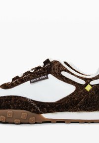 Adidași cu un upper texturat maro, detalii din piele albă și o talpă din cauciuc maro. Prezintă un eticheta "Din 1984" și un accent galben.