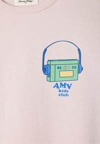 Šviesiai rožinė marškinėliai su žalia kasetės grotuvo grafika ir mėlynomis detalėmis bei tekstu „AMV vaikų klubas“ mėlynai apačioje.