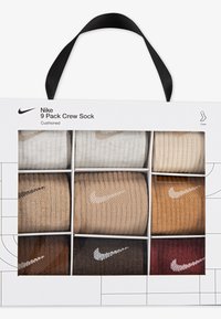 Devet parov crew nogavic, razstavljenih v beli škatli z črnim ročajem. Barve vključujejo bež, rjavo in bordo. Vsak par ima logotip Nike.