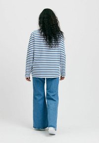 Valkoinen ja tummansininen raidallinen pitkähihaista paitaa, yhdistettynä leveälahkeisiin sinisiin farkkuihin, joissa on rento istuvuus ja kevyt materiaali.