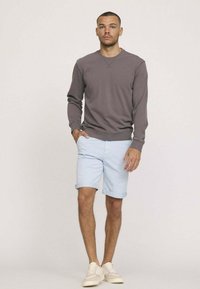 Sweat-shirt gris, shorts bleu clair, baskets beiges. Design décontracté avec des poignets et un ourlet côtelés, shorts roulés au bas. Style minimaliste.