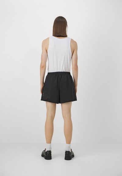 Black shorts with an elastic waistband, featuring side panel accents. Paired with a white tank top and black shoes.