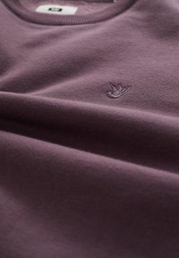 Lila sweatshirt i mjukt tyg, med ribbad halsringning och en broderad logotyp i en något mörkare nyans.