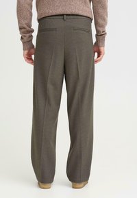 Wijduitlopende broek in olijfgroene stof, met een gestructureerde weving, plooien aan de voorkant en twee achterzakken met subtiele accenten.