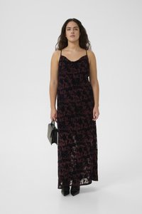 Maxi dress with thin straps, featuring a dark floral pattern in shades of burgundy and black. Model holding a small black handbag, wearing pointed shoes.