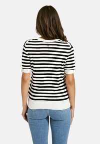 Black and white striped knitted sweater with short sleeves and a round neckline. Features a ribbed hem and subtle logo on the back.