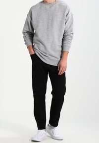 Sudadera gris de algodón con cuello redondo, puños y dobladillo acanalados, combinada con pantalones negros y zapatillas blancas. Colores lisos, ajuste informal.