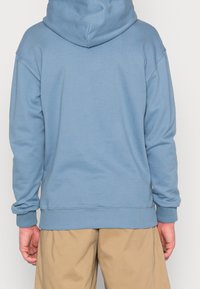 Sudadera con capucha de color azul claro, de manga larga, con puños y dobladillo acanalados. Presenta un ajuste holgado y está hecha de una suave mezcla de algodón.