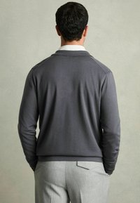 Grå pullover-sweater med ribbet krave, lange ærmer og en glat tekstur, parret med lysegule skræddersyede bukser.