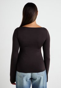 Maglietta a maniche lunghe in tessuto marrone scuro con scollatura ampia e quadrata e silhouette aderente, abbinata a jeans in denim azzurro chiaro.