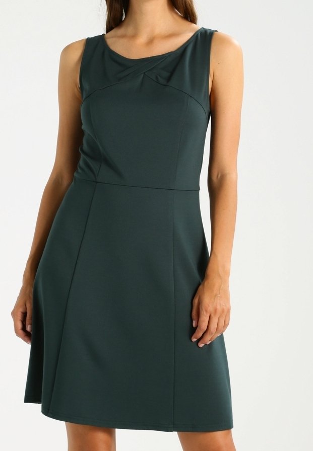 Robe verte sans manches en tissu lisse, avec un col rond, des détails froncés au niveau de la poitrine et un ourlet évasé.