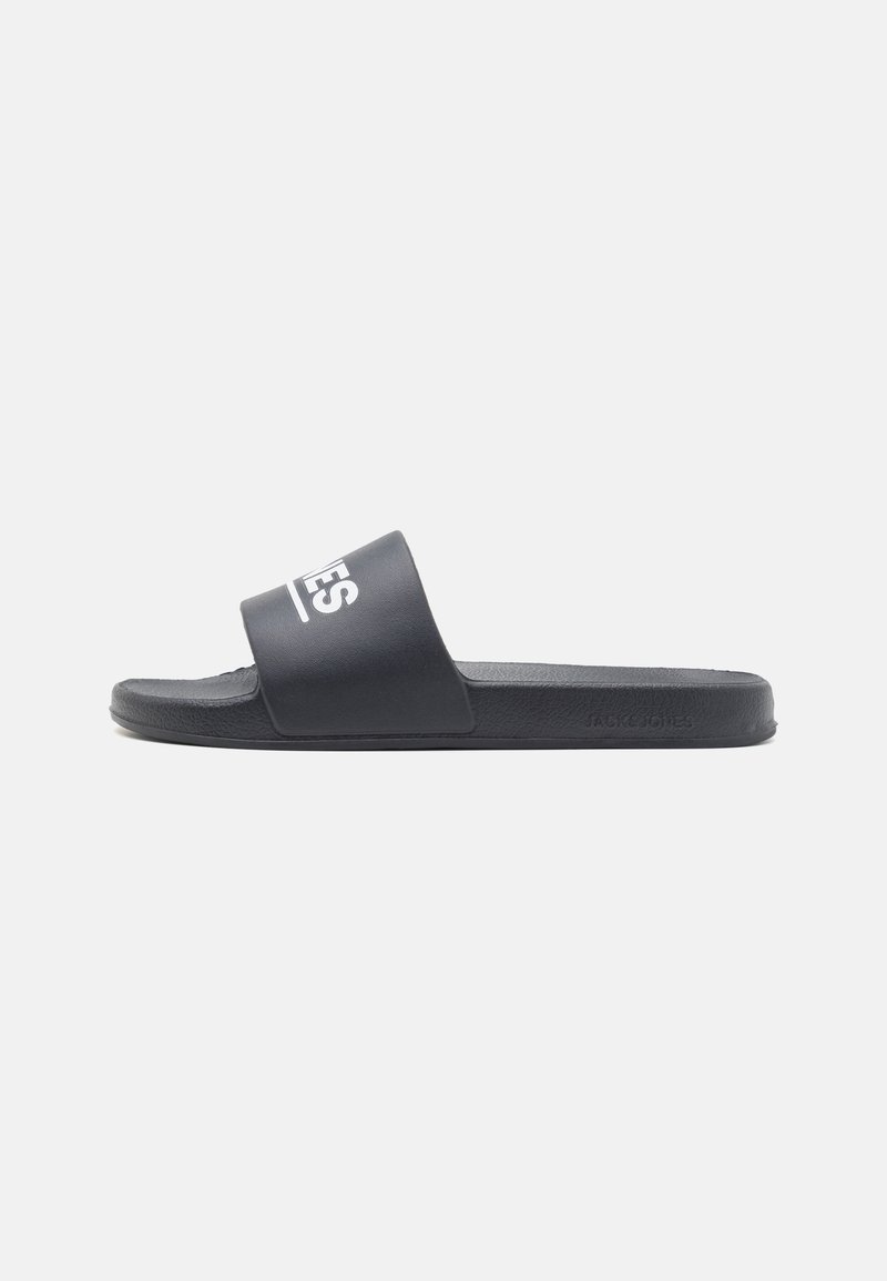 Black slide sandal with a wide strap featuring white branding. Made of rubber, it has a textured footbed for comfort and a flat sole.