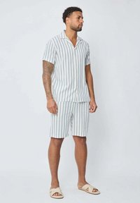 Chemise à manches courtes rayée et shorts assortis en mélange de coton bleu clair et blanc. Présente un col ouvert et une coupe décontractée, accompagnée de sandales beiges.