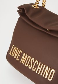Braune Lederhandtasche mit goldener Kettenriemen und "LOVE MOSCHINO" in großen goldenen Buchstaben auf der Vorderseite geprägt.