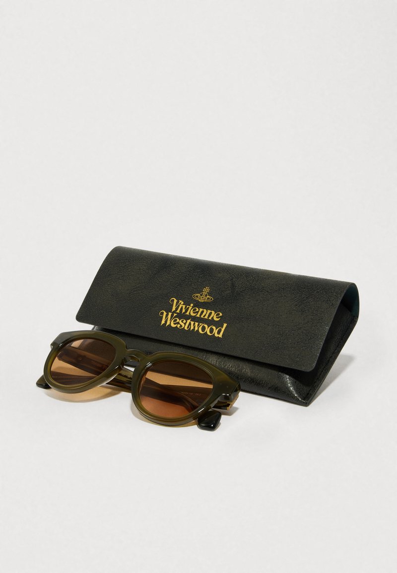 Olive green sunglasses with brown lenses, featuring rounded frames, sit beside a black leather case with gold "Vivienne Westwood" logo.