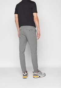 Grijze, gestructureerde broek met een slim fit, voorzien van twee achterzakken, gedragen met een zwart shirt met korte mouwen en grijze sportieve schoenen.