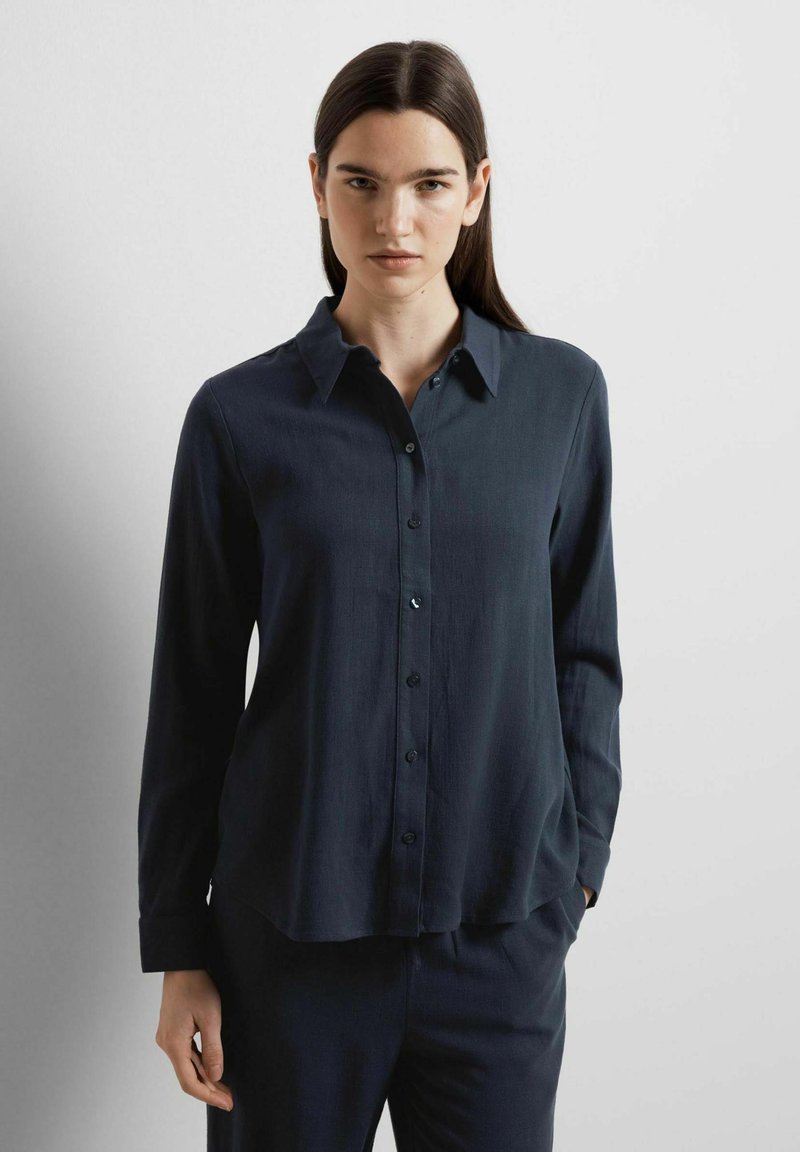 Dark navy button-up shirt with long sleeves, a classic collar, smooth texture, and a curved hem; features front button closure.