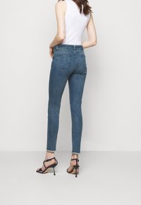Höga, urtvättade blå skinny jeans med rå fåll, med bakfickor, som är kombinerade med svarta remsandaler och en vit linnetopp.