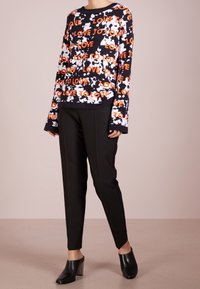 Haut noir à manches longues avec motif de texte "LOVE TO LOVE" en blanc et orange, associé à un pantalon noir ajusté et des mules à talons noires.