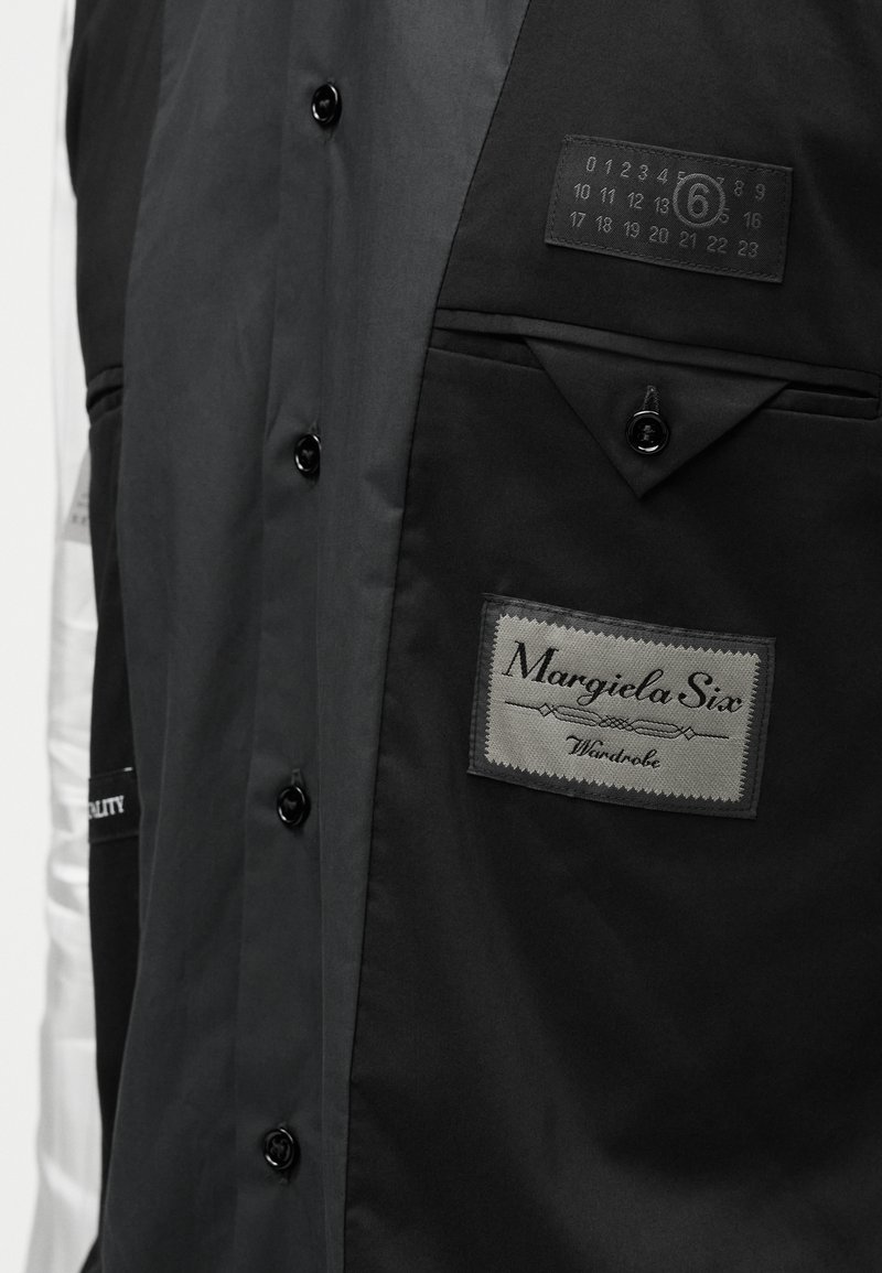 Svart flerpanskjorta med knappstängning och fickor. Har en tygetikett, tryckta motiv och en mjuk textur. Silverdetaljer på ärmen.