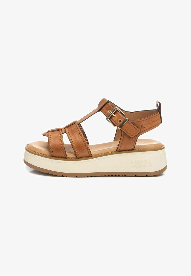 Sándalo de cuero marrón con diseño de tiras, hebilla ajustable y una suela gruesa de plataforma blanca. Plantilla de color marrón claro y suela exterior texturizada.