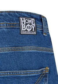 Džinsai su mėlynu audiniu. Turi juodą stačiakampį etiketę su užrašu "HOME BOY" ir "loud-couture" baltu tekstu. Geltoni siuvinėjimo detalės.