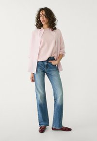 Lys pink skjorte med knapper over en matchende top, kombineret med mid-rise blå jeans og burgunder sko. Bløde teksturer og afslappet pasform.