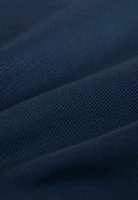 Sötétkék szövet finom bordázott textúrával és gyengéd redőkkel, amelyek lágy árnyékokat és kiemeléseket hoznak létre.