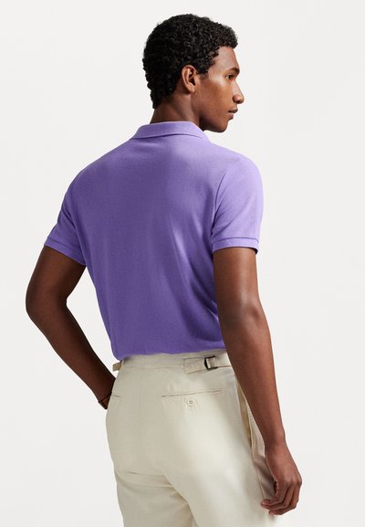 Vijolična polo majica z teksturirano tkanino, kratkimi rokavi in ovratnikom, v kombinaciji s kremnimi elegantnimi hlačami, ki imajo zadnji žep.